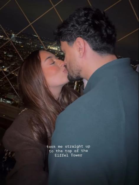 A couple kissing at the top of the Eiffel Tower at night.