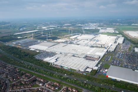 Aerial view of a large factory complex with surrounding parking lots and wind turbines.