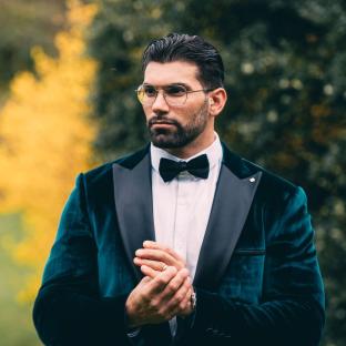 Man in teal velvet tuxedo adjusting his ring.