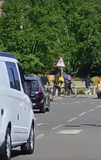 People crossing a street near parked cars and a cyclist.