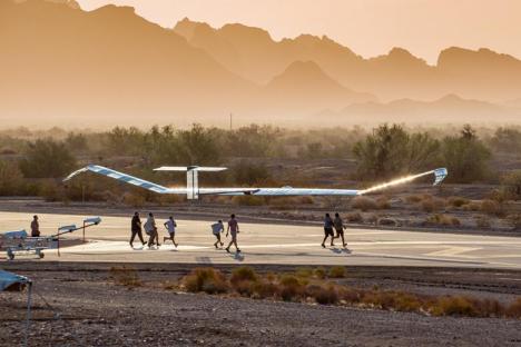A solar-powered aircraft on a desert runway with people walking nearby.