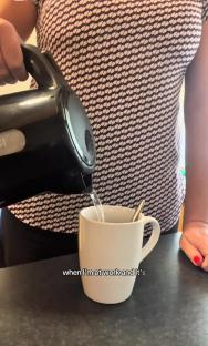 Person pouring hot water from an electric kettle into a mug.