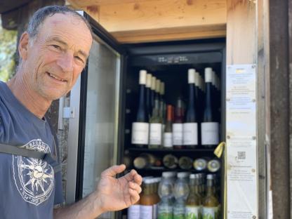 Man standing by an outdoor honesty fridge stocked with drinks and wine.
