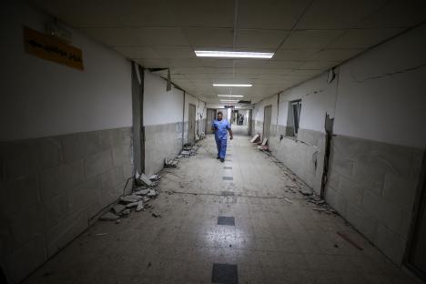 Destroyed hospital hallway with debris and a person walking through.