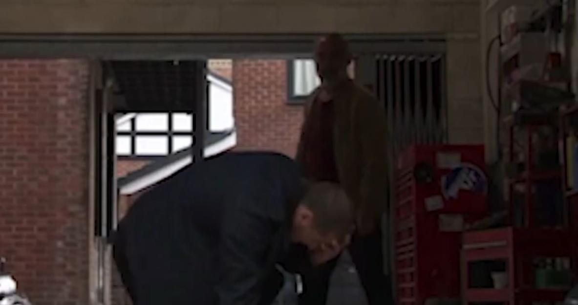 A man bending over in a garage with another man standing behind him.