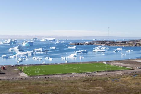 Soccer field in Qeqertarsuaq, Greenland, with icebergs in the background.