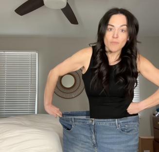Woman holding up large, loose jeans after weight loss.
