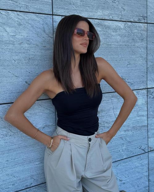 Woman in sunglasses and a black tank top leaning against a wall.