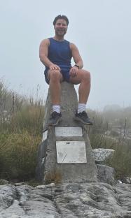 Man sitting on a summit marker.