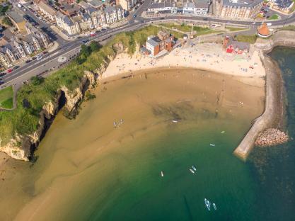 Aerial view of Cullercoats beach with people swimming and paddleboarding.