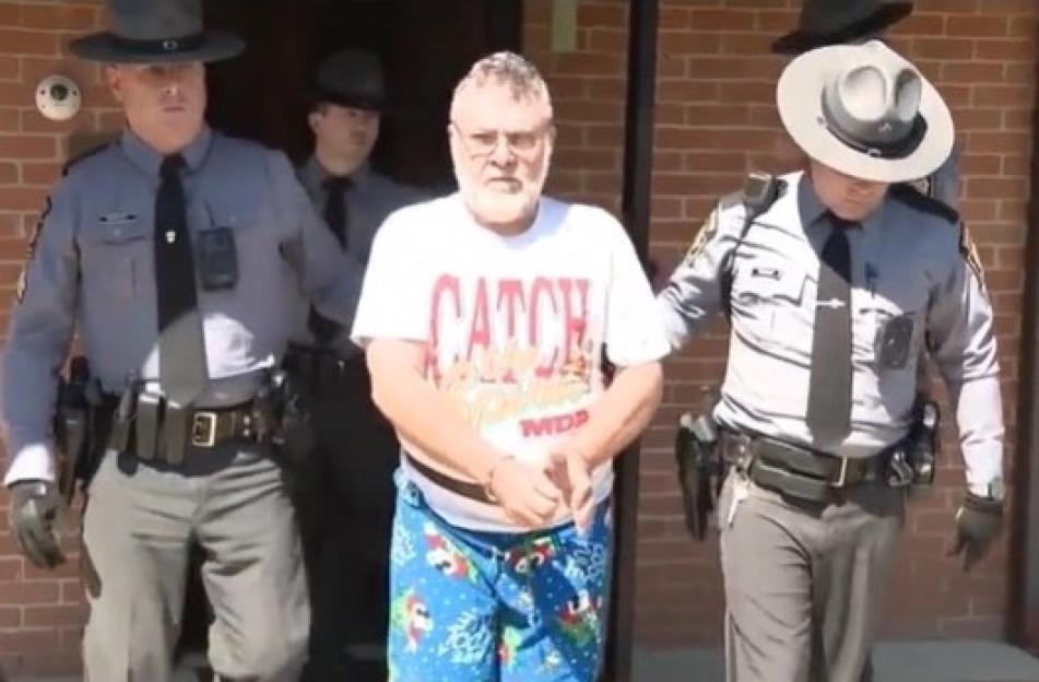 A handcuffed man in pajama shorts being escorted by police officers.