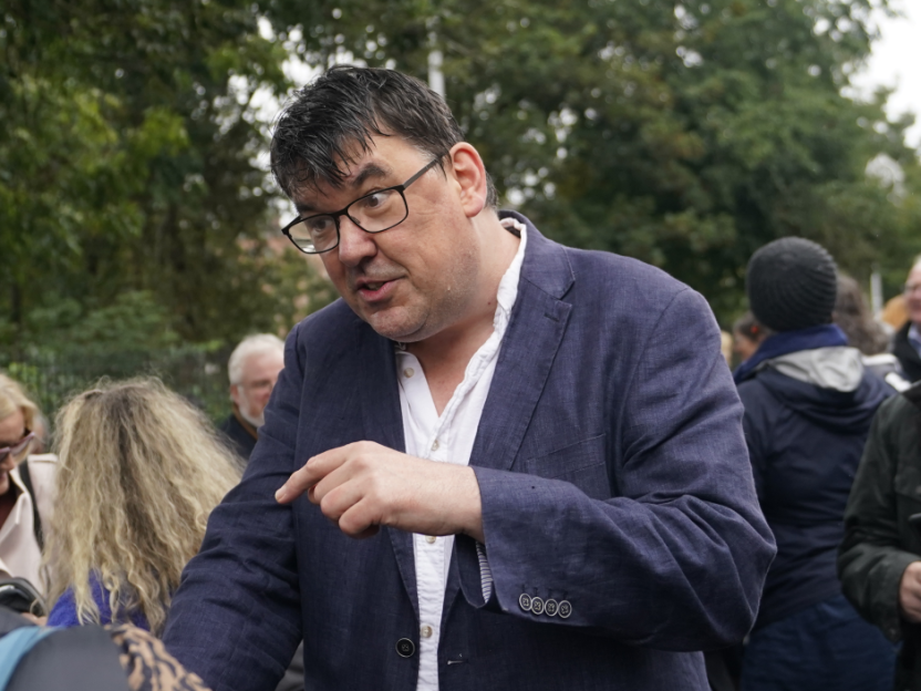 Man in glasses giving a speech outdoors.