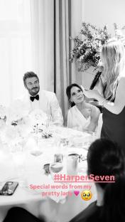 Black and white photo of David and Victoria Beckham at a table, listening to a woman giving a speech.
