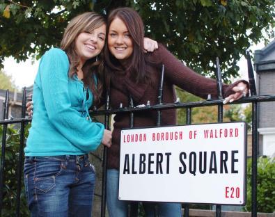 Louisa Lytton and Lacey Turner, actors from Eastenders, posing by an Albert Square street sign.