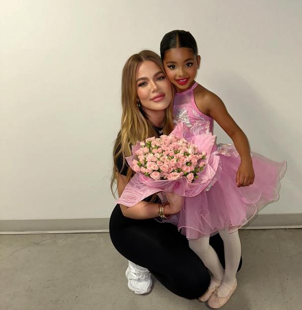 Khloe Kardashian with her daughter True, who is dressed in a pink ballet costume and holding a bouquet of pink roses.