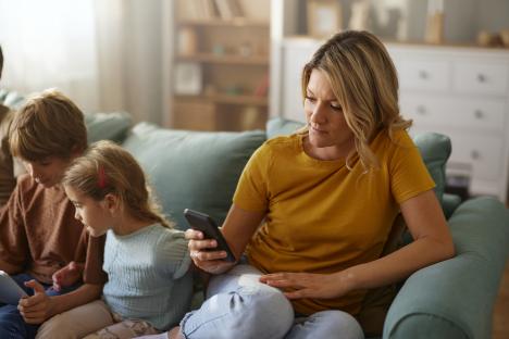 Mother text messaging on her phone while sitting on a couch with her children.