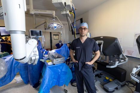 Surgeon standing in operating room with robotic surgery equipment.