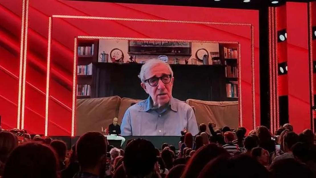 Woody Allen speaking on a large screen at a film festival.