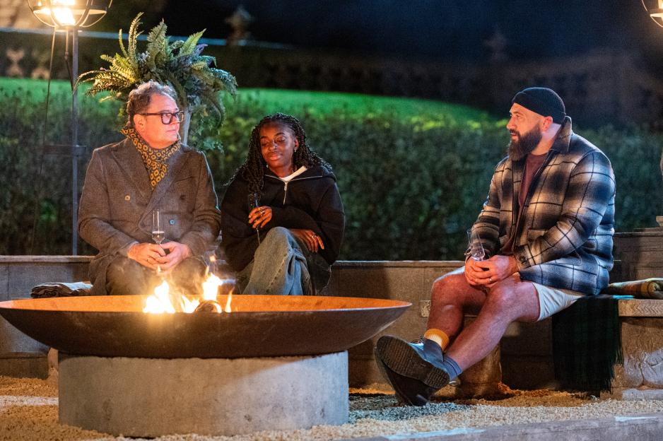 Three people sit around a fire pit outdoors at night.