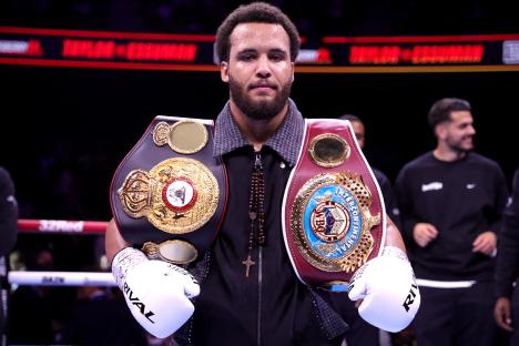 Moses Itauma holding two championship belts after a boxing victory.