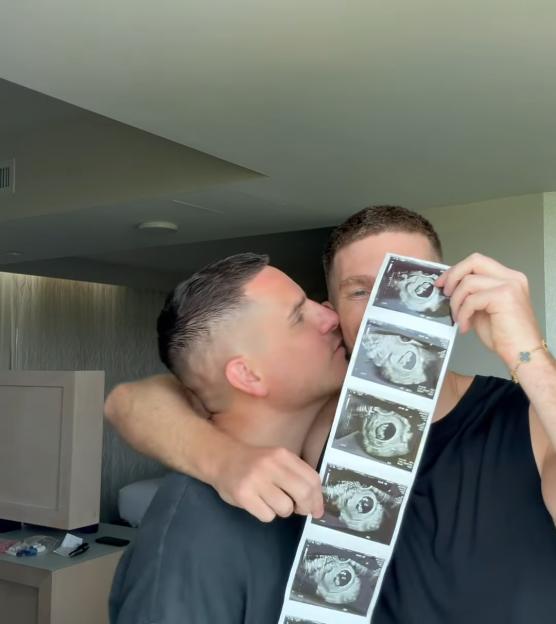 Two men kissing while holding up a series of ultrasound images.