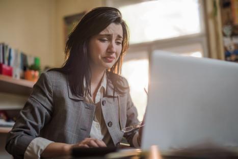A young businesswoman crying while working on her laptop.