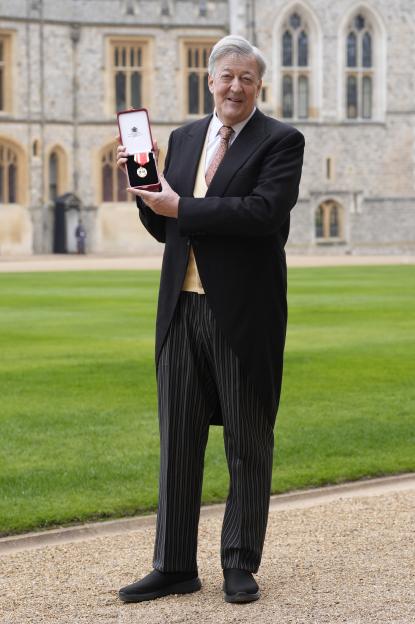 Sir Stephen Fry holding his knighthood medal at Windsor Castle.