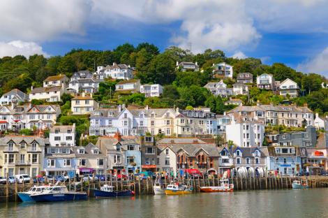 Looe harbor in Cornwall, UK, with colorful houses on a hillside and boats in the harbor.