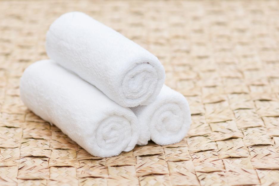 Three rolled white towels on a woven mat.