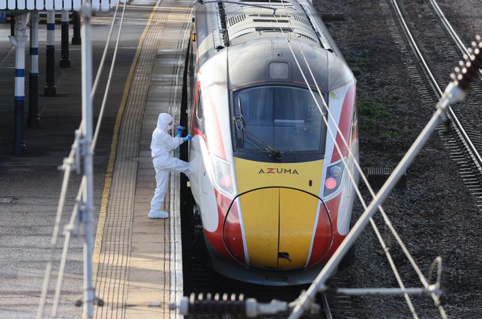 A forensic officer in a white suit inspecting an Azuma train at a station platform.