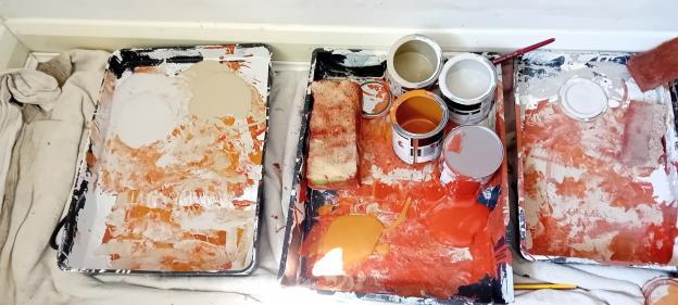 Three paint trays with leftover paint and paint cans.