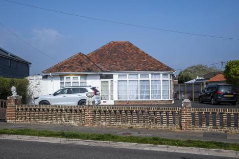 A bungalow with a red tile roof and a large bay window. A silver SUV is parked in front.