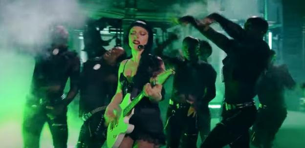 Lady Gaga playing guitar on stage with backup dancers.