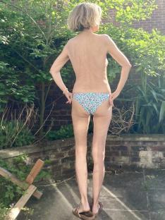 Woman in floral bikini bottoms standing with her back to the camera in a garden.