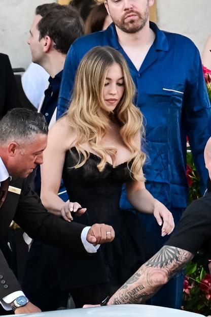 Sydney Sweeney in a black dress with two men on either side of her, one in a suit and the other in a blue pajama top.