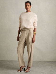 Woman wearing a cream sweater, beige trousers, and white heels.
