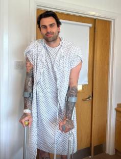 Man in hospital gown using crutches.