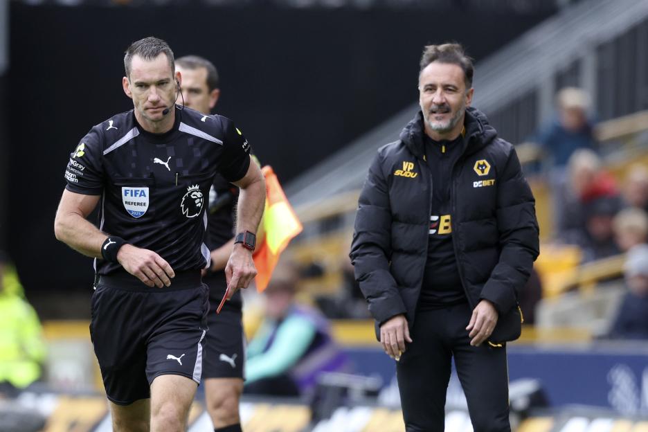 Referee Jarred Gillett holding a red card while standing near Wolverhampton Wanderers manager Vitor Pereira.