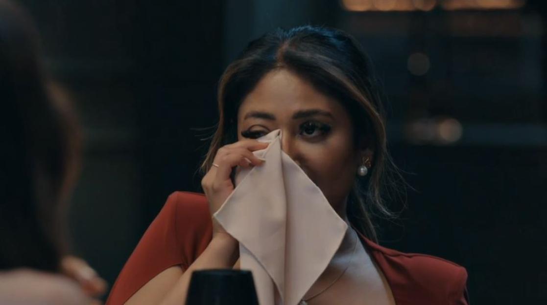 Nelly weeping at a dinner party, wiping her face with a napkin.