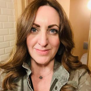 Photo of Mel Coloma, a woman with long brown hair, wearing a green jacket.