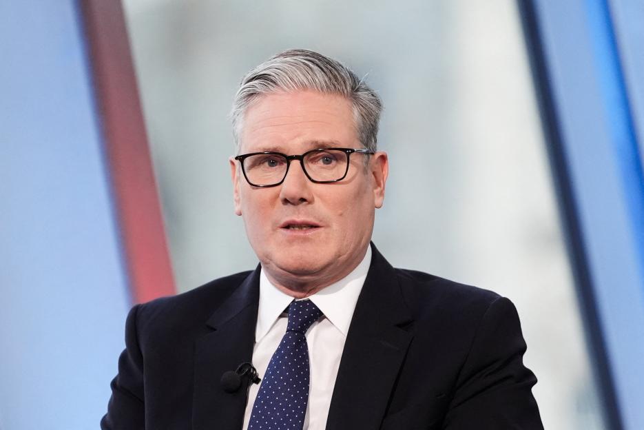 British Prime Minister Keir Starmer wearing glasses, a dark suit, white shirt, and a spotted blue tie.