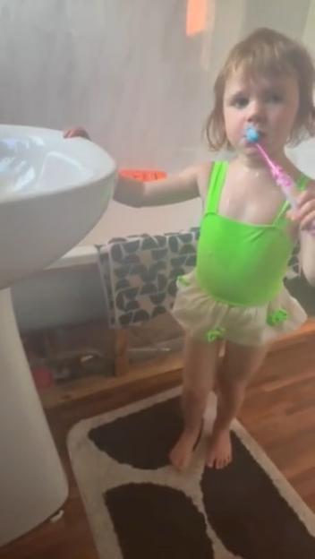 Teraysa, a three-year-old girl, brushing her teeth while wearing a bright green bathing suit.
