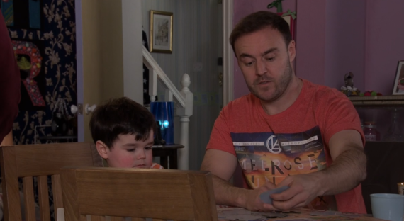 Screenshot of a man and a young boy sitting at a table, playing cards.