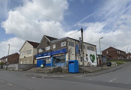 Photo of a street scene with a fish bar, convenience store, and a mural.