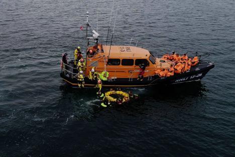 An image collage containing 1 images, Image 1 shows RNLI lifeboat crew rescuing migrants in the English Channel