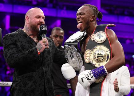 KSI celebrates a boxing victory, holding championship belts.