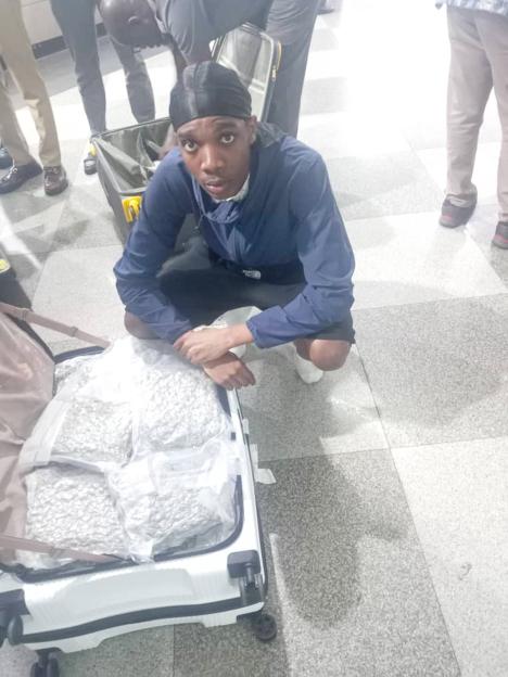 A young man kneels beside a suitcase full of cannabis.