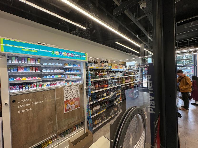 Interior view of a Tesco Express store with alcohol and cigarettes behind protective barriers.