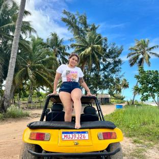 Woman sitting on a yellow dune buggy in front of palm trees.