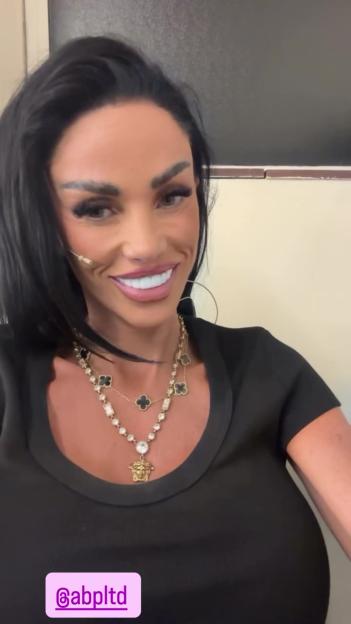 Katie Price smiling while wearing a black shirt and layered necklaces.